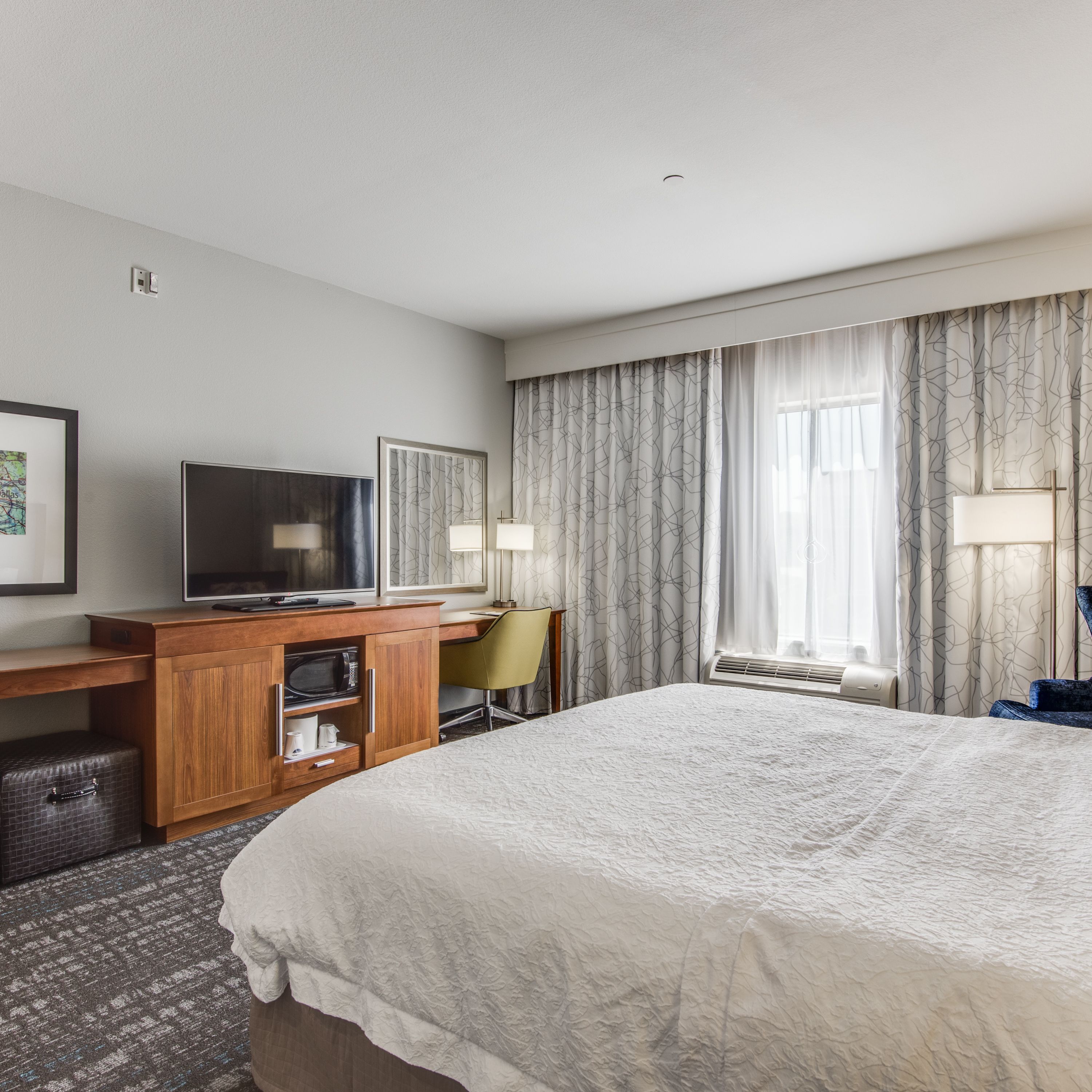 Habitación de hotel con una cama grande, un escritorio, un televisor de pantalla plana, una silla y una ventana con cortinas.