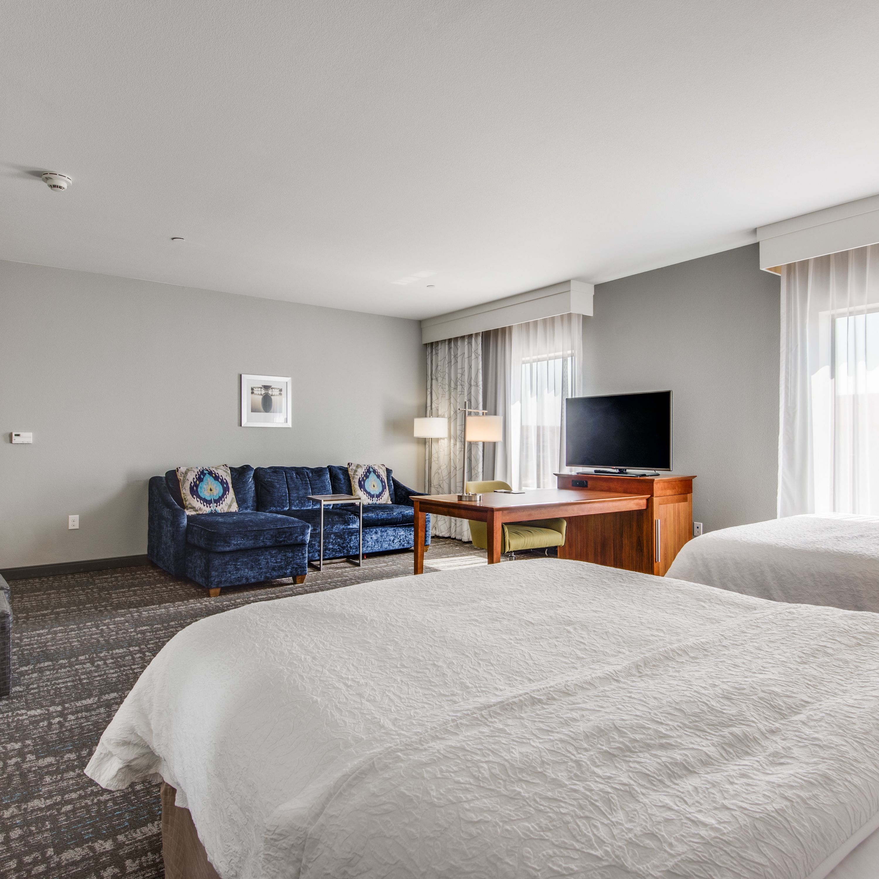 A hotel room with two beds, a sofa, a desk, and a TV.