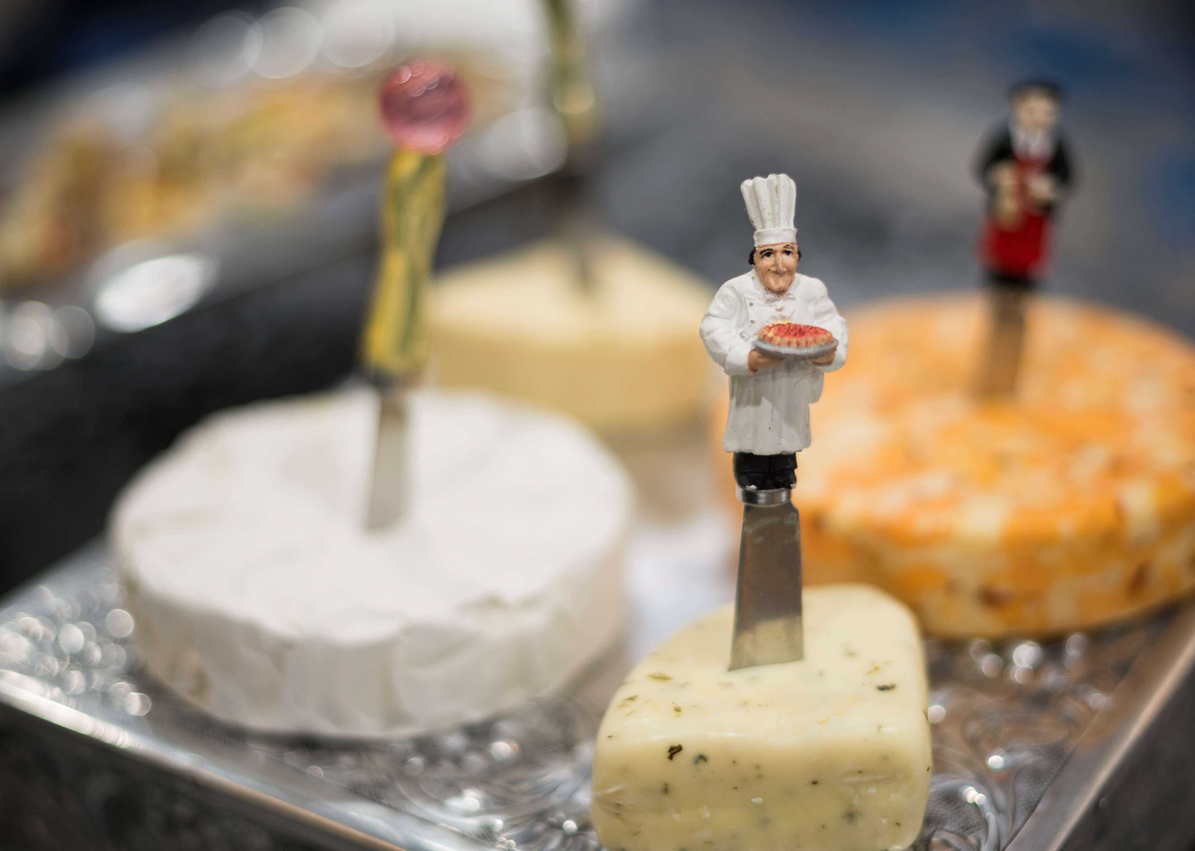 Una exhibición de postres con figuritas de chefs en miniatura encima de cada uno.