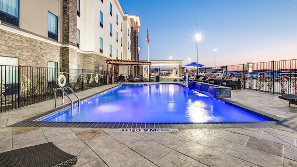 A hotel pool area with a clear blue pool, a covered seating area, and a flagpole with an American flag.