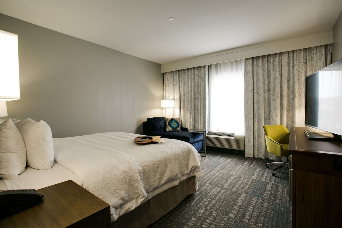 Une chambre d’hôtel avec un grand lit, un bureau, une chaise, une lampe et un téléviseur.