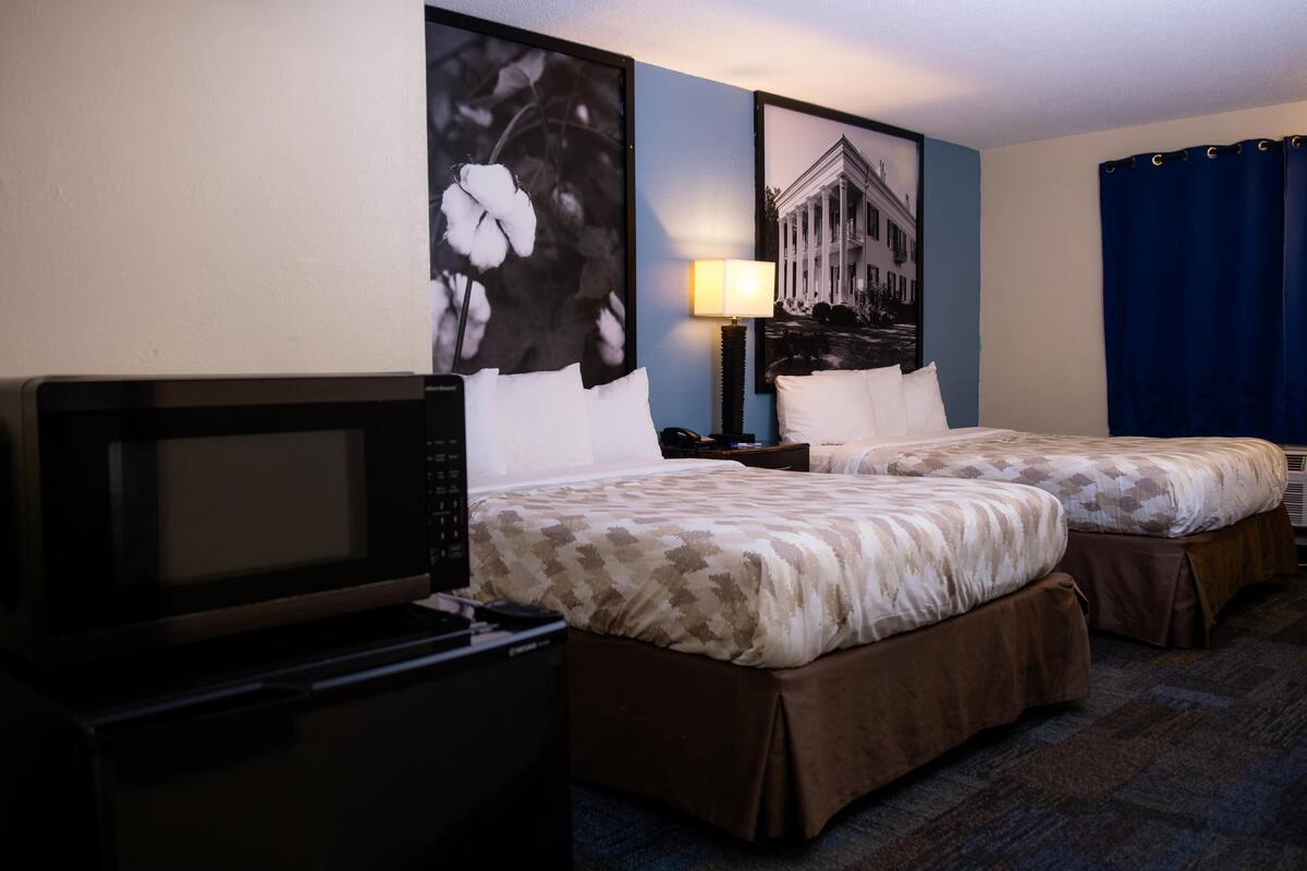 A hotel room with two beds, a TV, a lamp, and framed pictures on the wall.
