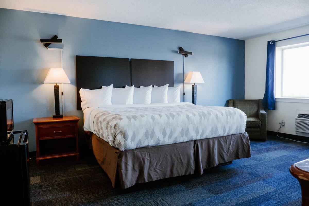 A hotel room with a large bed, two bedside tables with lamps, a chair, and a window with curtains.