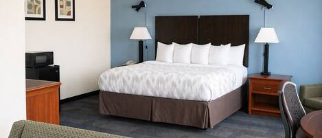 A hotel room with a bed, two bedside tables, a desk with a microwave, a chair, and a couch.