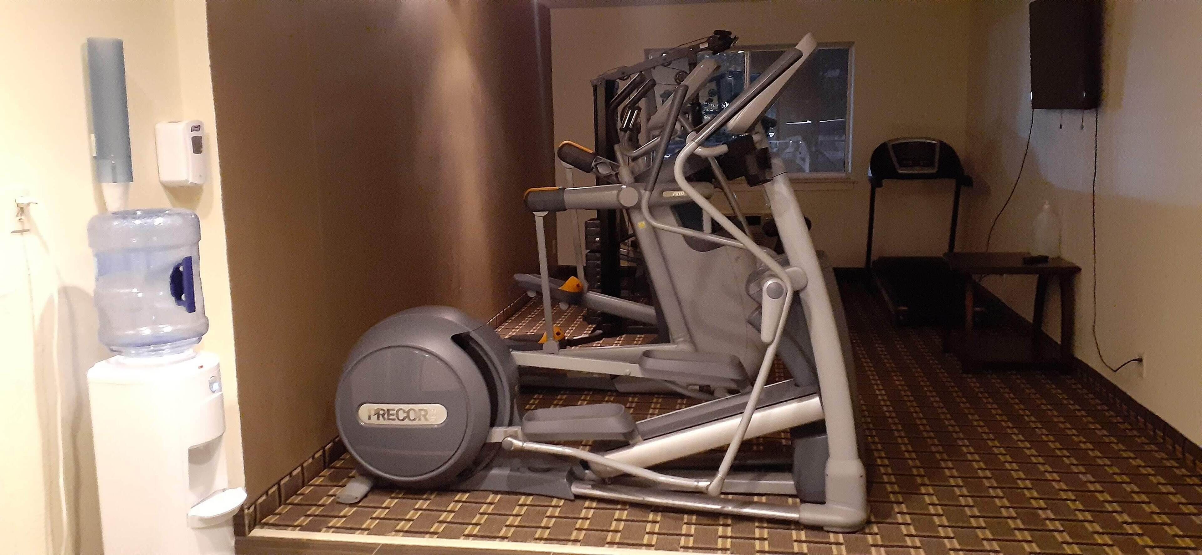 Un gimnasio con dispensador de agua, equipo de ejercicio y suelo estampado.