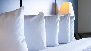 A neatly made bed with white bedding and pillows, a lamp on the side, and a dark-colored wall in the background.