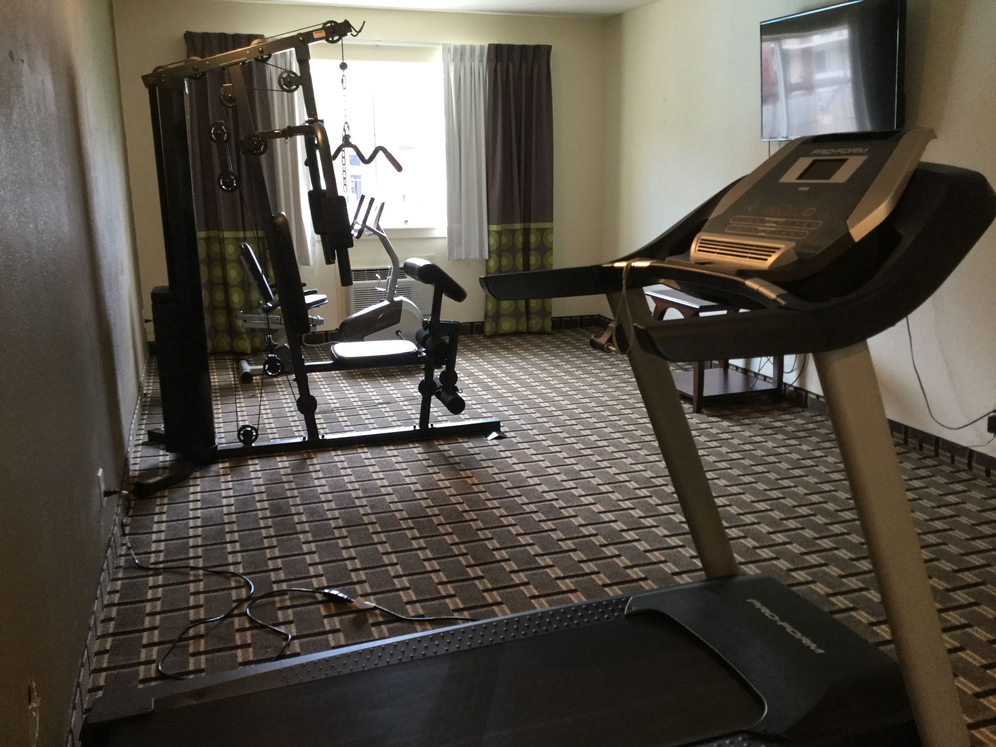 A gym with a treadmill, weight machine, and a TV in the background.