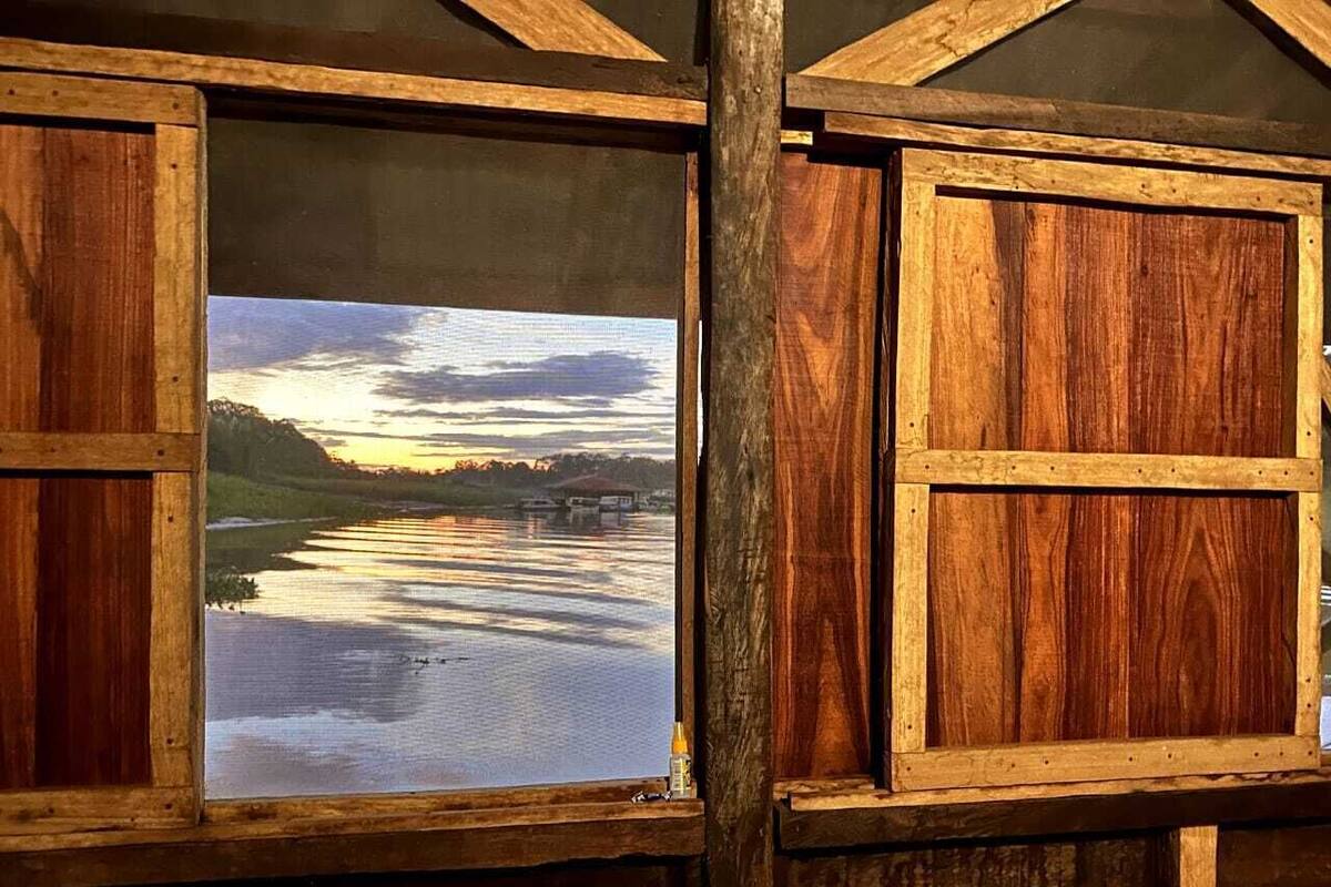 Une cabane en bois dotée d’une grande fenêtre donnant sur un lac paisible au coucher du soleil.