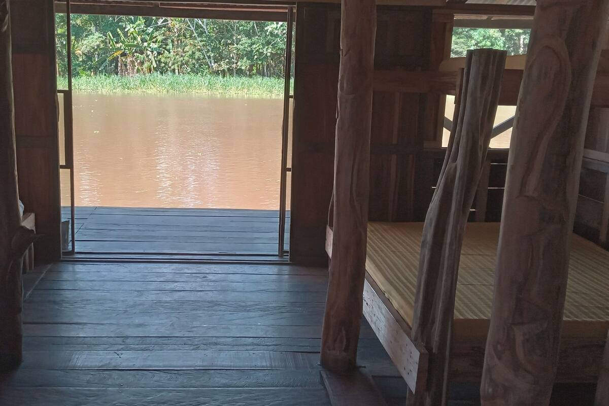 Un couloir en bois mène à un plan d’eau, avec un lit placé à gauche et une structure en bois à droite.