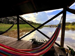 A hammock under a wooden structure with a view of a calm river and greenery. - Kurupira Cabin Floating (Leticia)