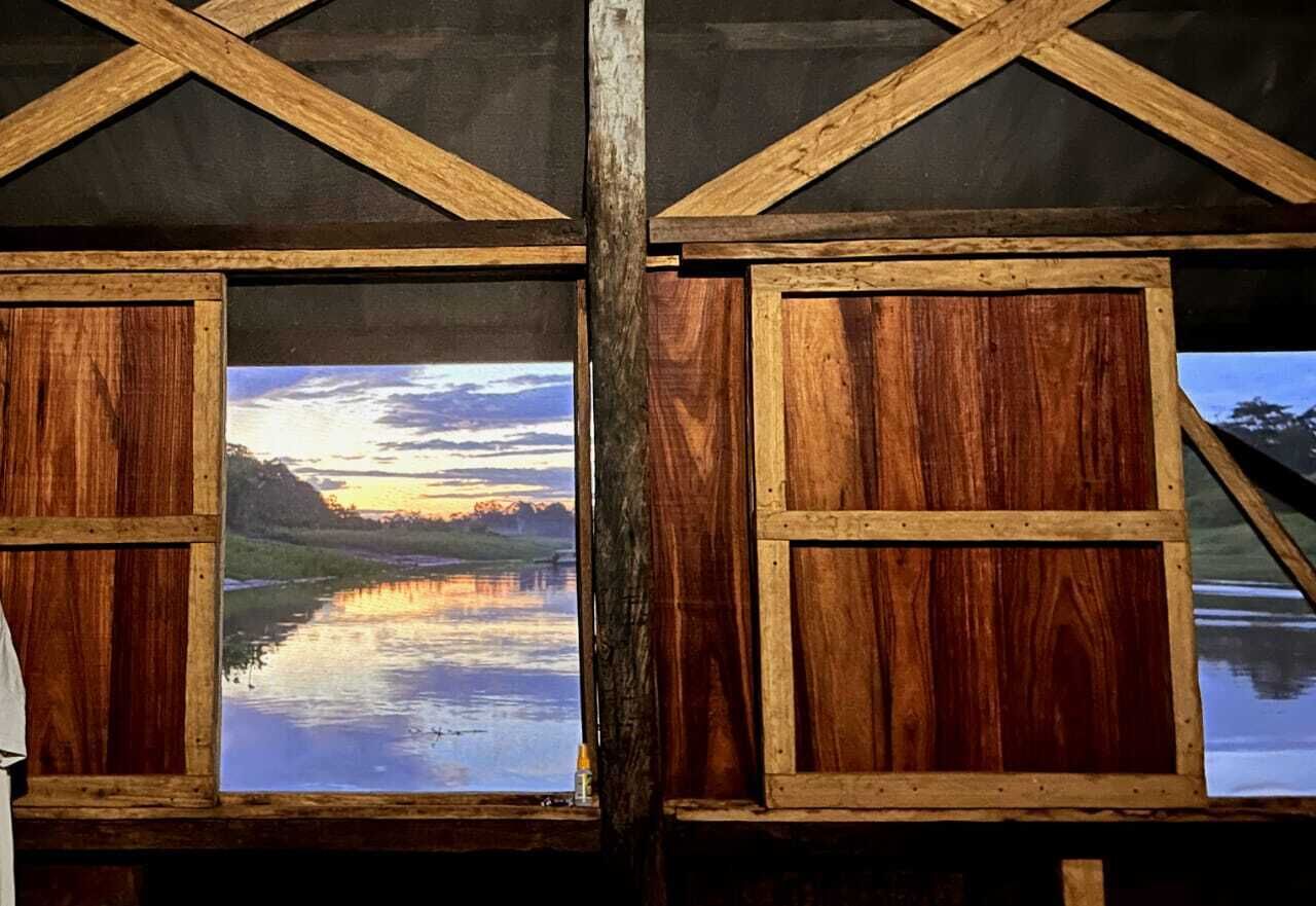 Una cabaña con paredes de madera y un amplio ventanal que refleja un atardecer sobre el agua.