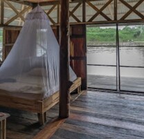 Una cama de madera con mosquitera, ventanas amplias y vistas al río.