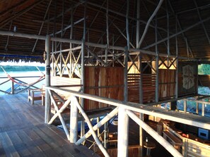 A wooden deck with a thatched roof, wooden railings, and a view of the water. - Kurupira Cabin Floating (Leticia)