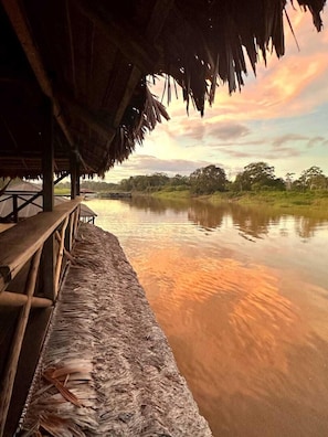 A thatched-roof structure with a wooden bench overlooking a calm river. - Kurupira Cabin Floating (Leticia)