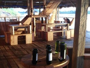 A wooden deck with tables and chairs, and three bottles on a table. - Kurupira Cabin Floating (Leticia)