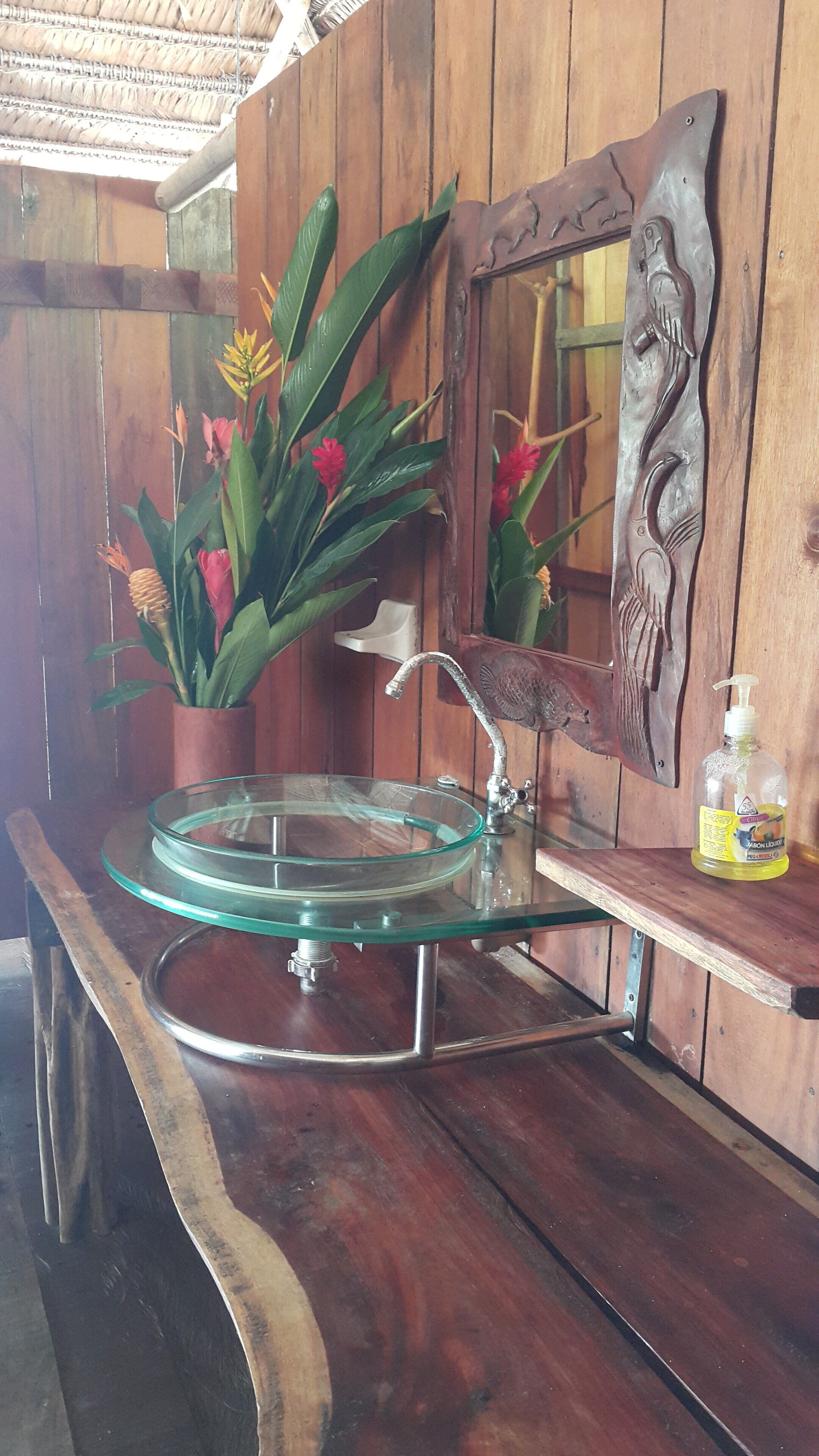 Een houten wastafelmeubel met een glazen wastafel, een spiegel en een decoratieve plant.