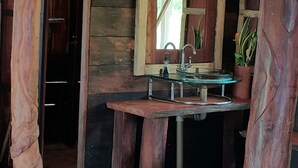 A rustic wooden bathroom with a glass sink, wooden walls, and a mirror. - Kurupira Cabin Floating (Leticia)