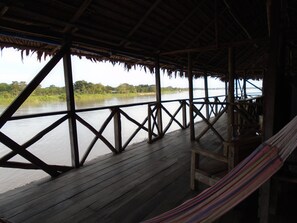 A wooden deck with a view of a calm river and greenery in the background. - Kurupira Cabin Floating (Leticia)