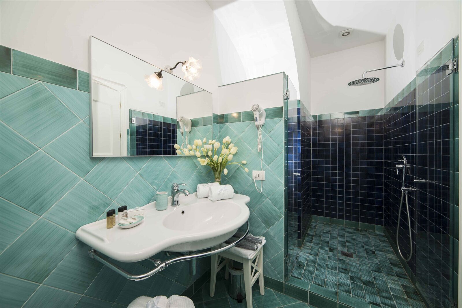 A bathroom with a white sink, mirror, and a shower with dark tiles.