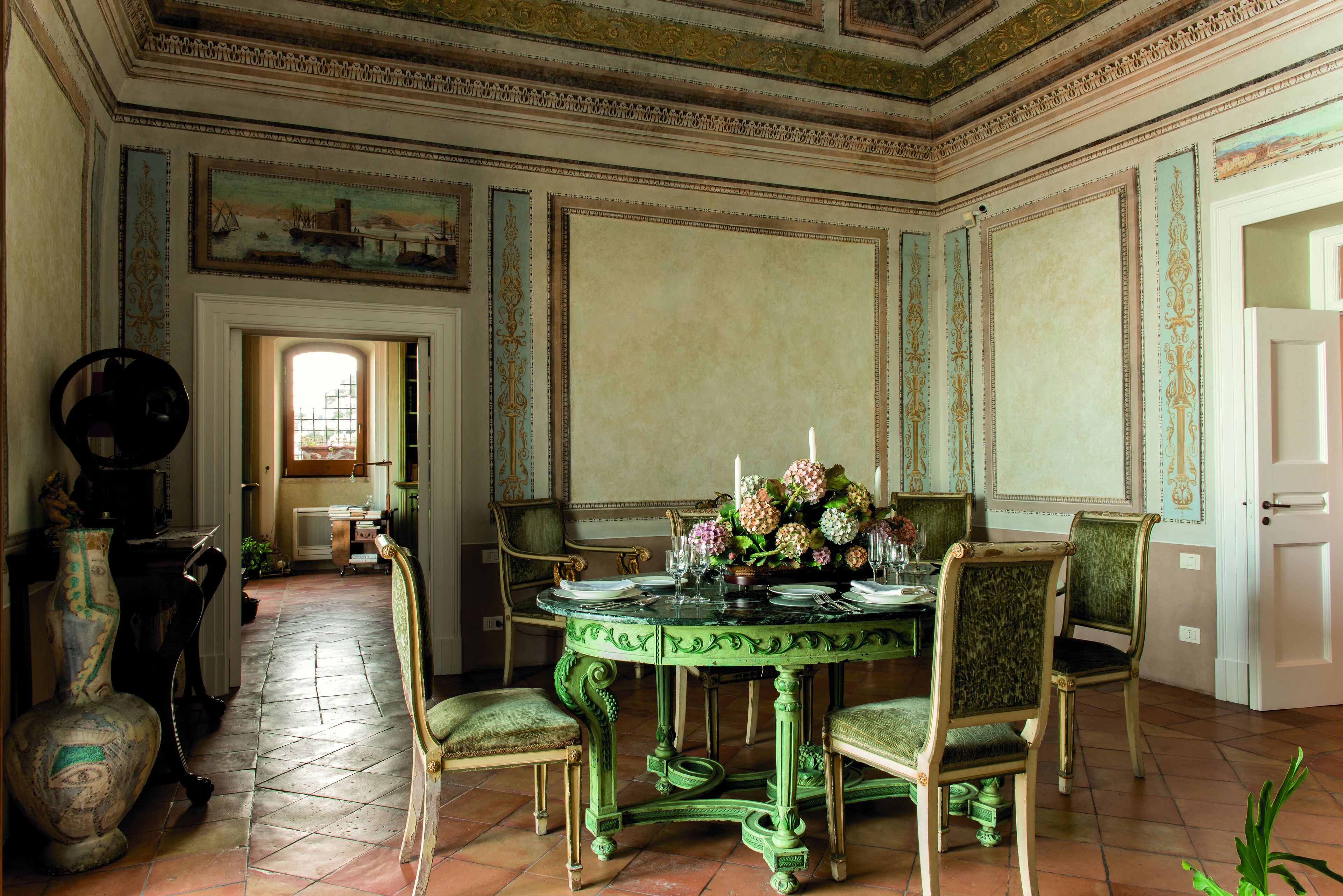 A dining room with a green table, chairs, and a vase of flowers.