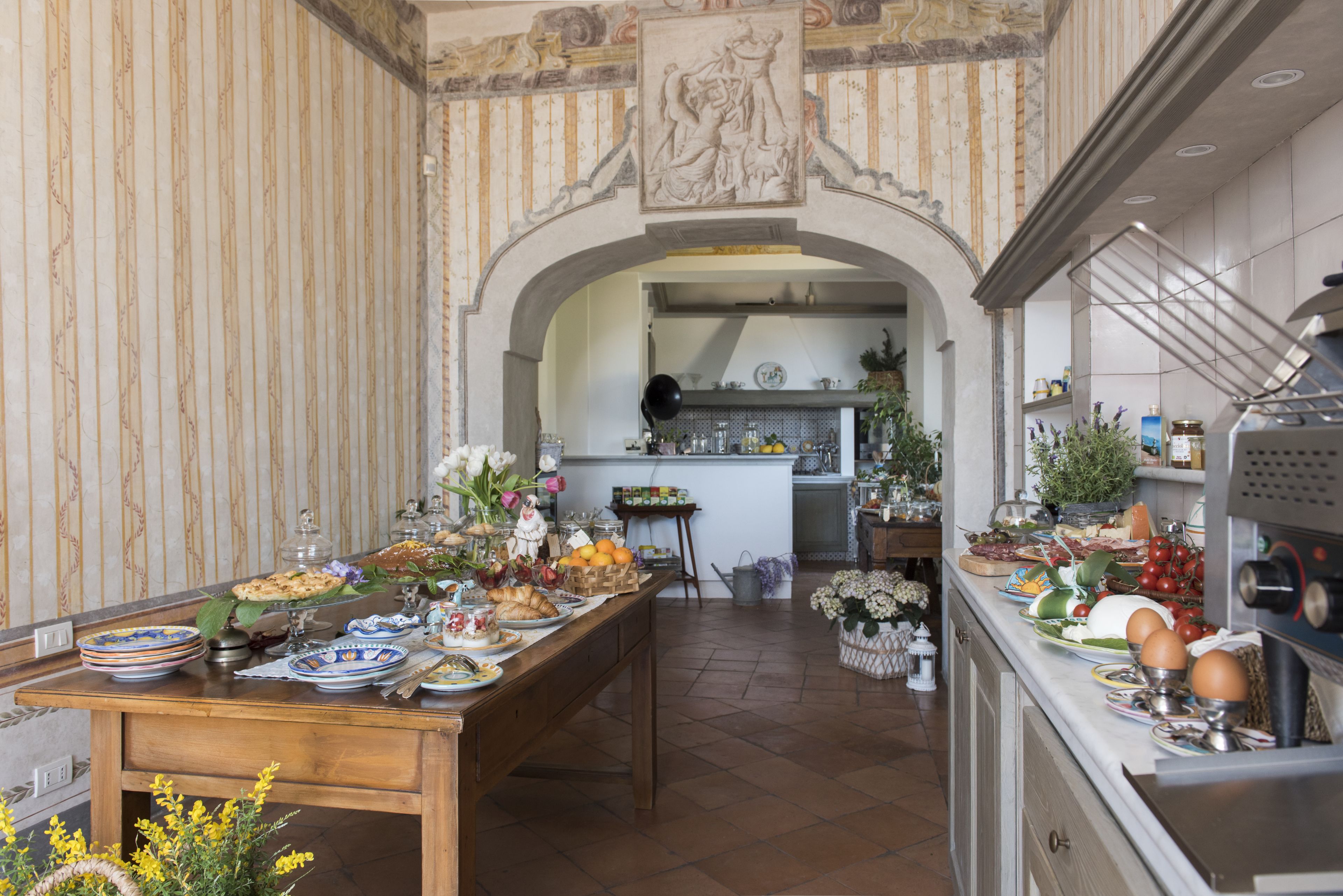 Un comedor con una mesa larga dispuesta para una comida, una cocina al fondo y un arco decorativo.