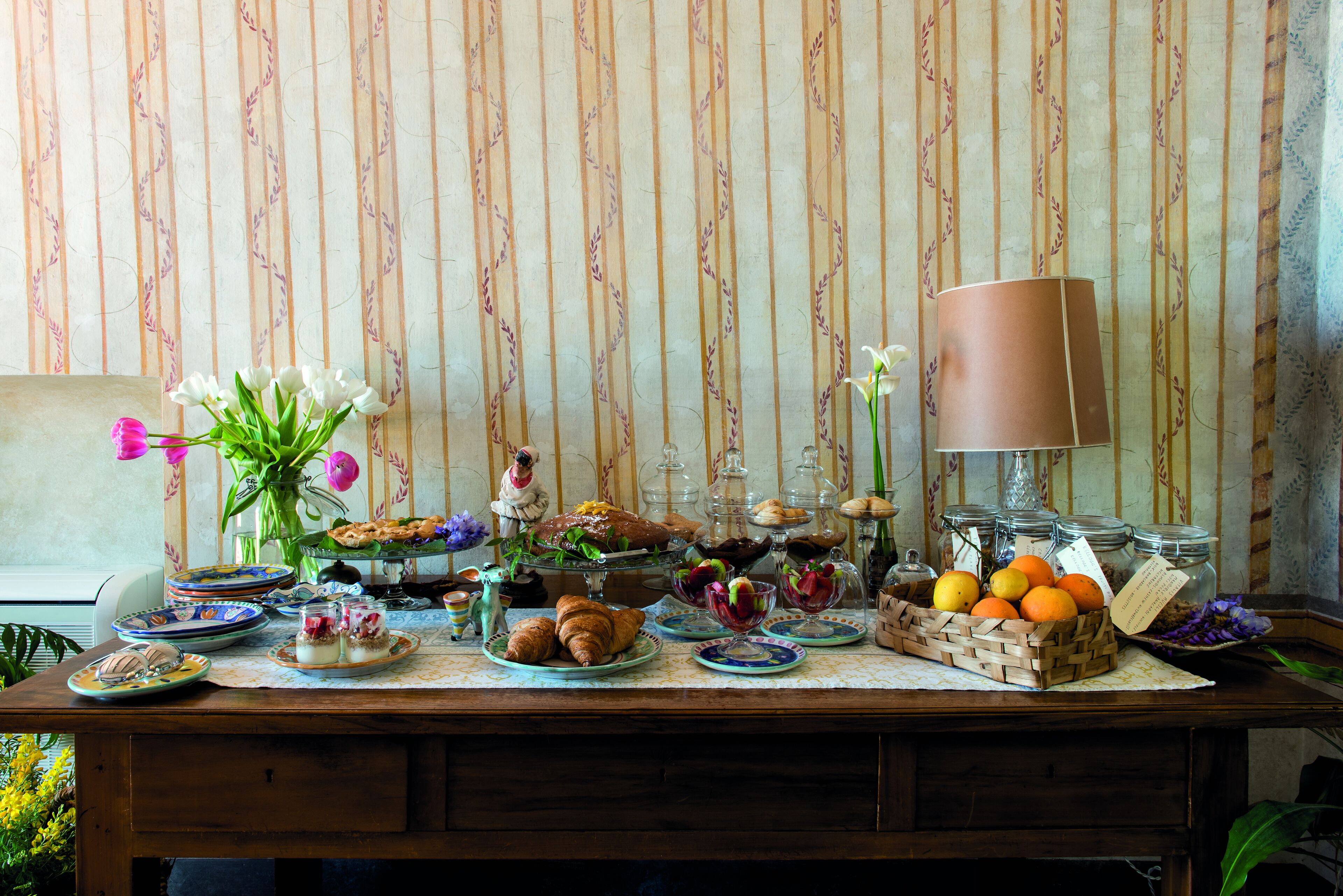 A table set with various pastries, fruits, and a vase of flowers.