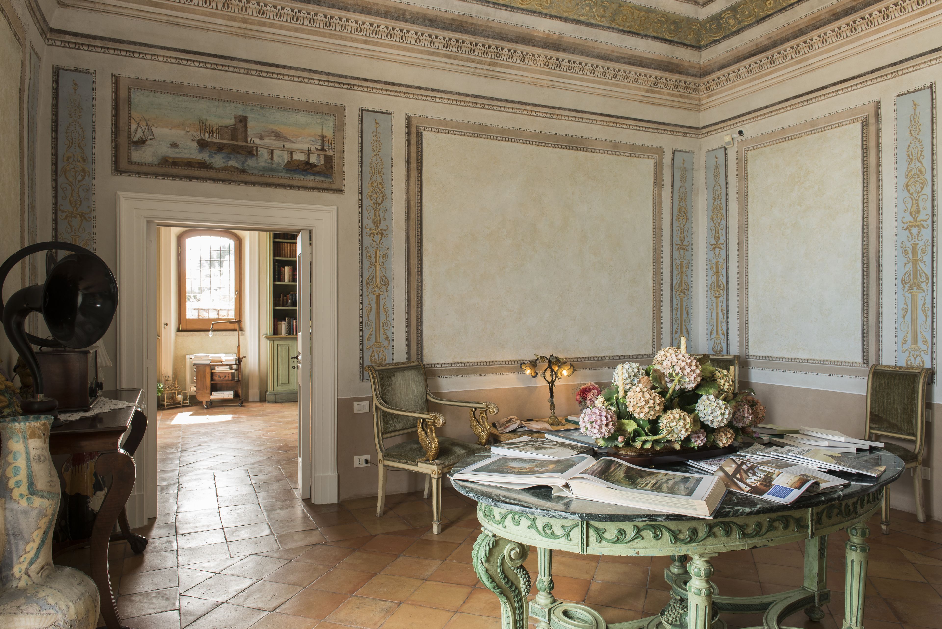 A room with a marble table, books, a vase of flowers, and a painting on the wall.
