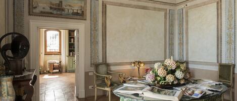 A room with a marble table, books, a vase of flowers, and a painting on the wall.