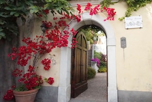 An arched entrance with a wooden door, surrounded by red bougainvillea flowers and a sign reading "Palace Arano". - Palazzo Suriano Amalfi Coast (Vietri sul Mare)