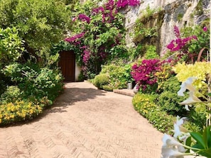 A paved pathway leading to a wooden door, surrounded by lush greenery and vibrant flowers. - Palazzo Suriano Amalfi Coast (Vietri sul Mare)