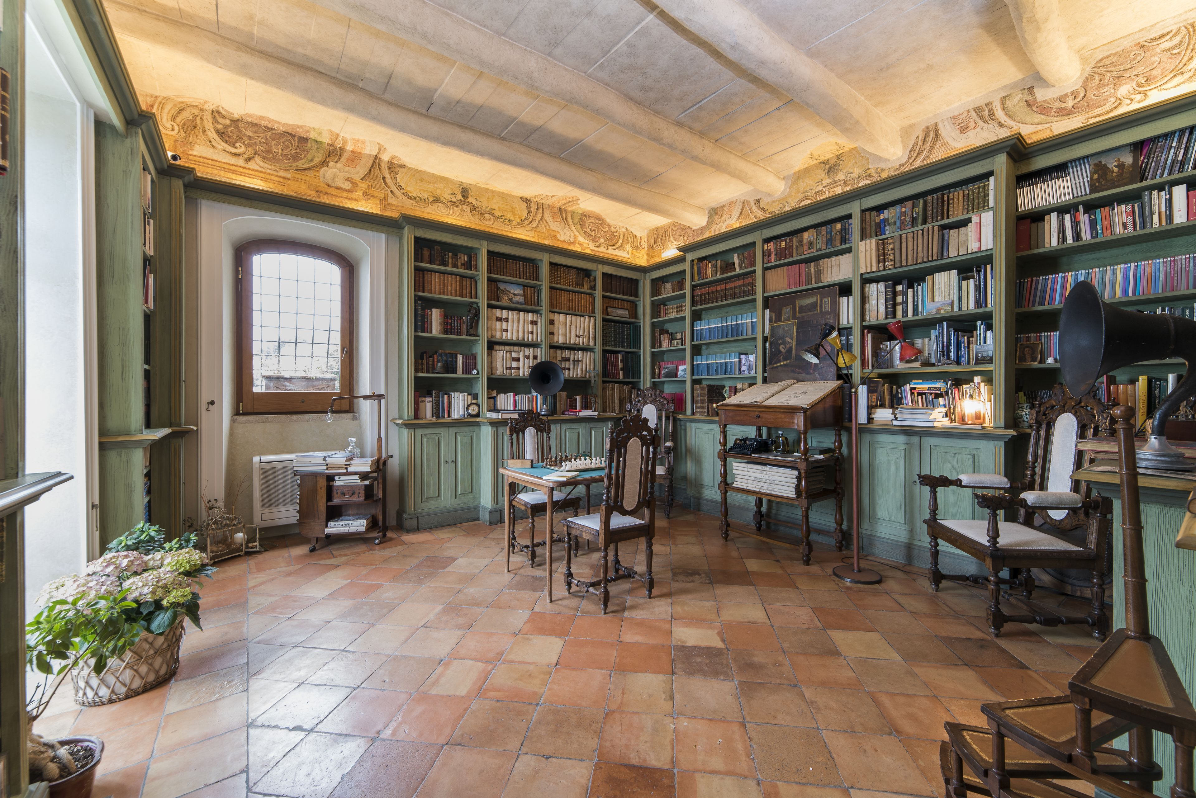 A library with green bookshelves, a chessboard, and a large window.