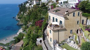 A coastal building with a balcony overlooking the sea, a narrow street, and lush greenery. - Palazzo Suriano Amalfi Coast (Vietri sul Mare)