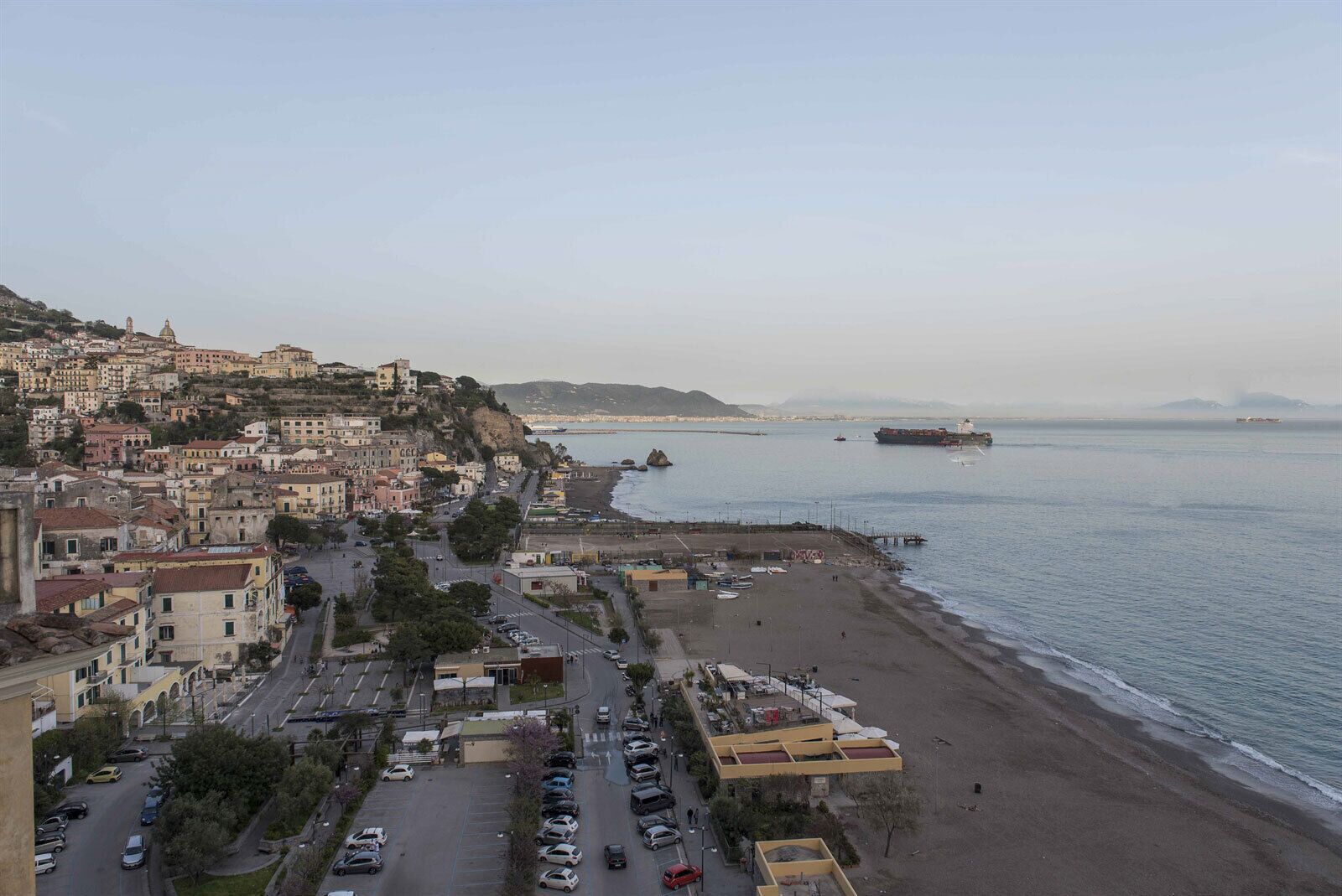 A coastal town with a beach, buildings, and a large ship in the distance.