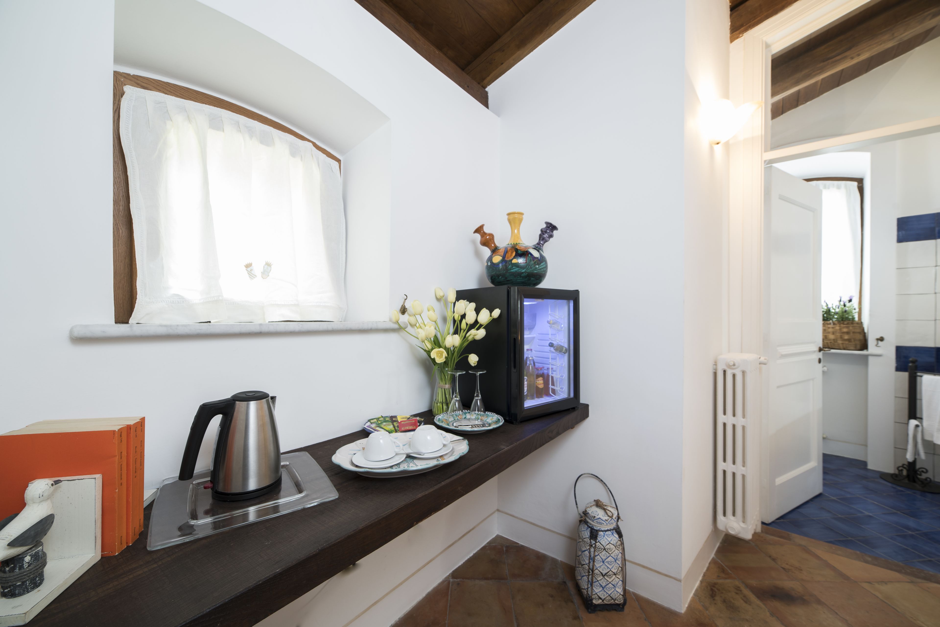 A kitchen with a window, a coffee maker, a vase with flowers, and a framed picture on the counter.