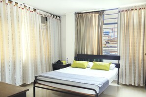 Une chambre d’hôtel avec un lit, une table de chevet, une fenêtre avec des rideaux et une vue sur les bâtiments environnants.
