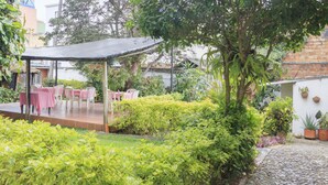 An outdoor patio with tables and chairs, surrounded by greenery and a cobblestone path. - Hotel Colonial Plaza (Bucaramanga)