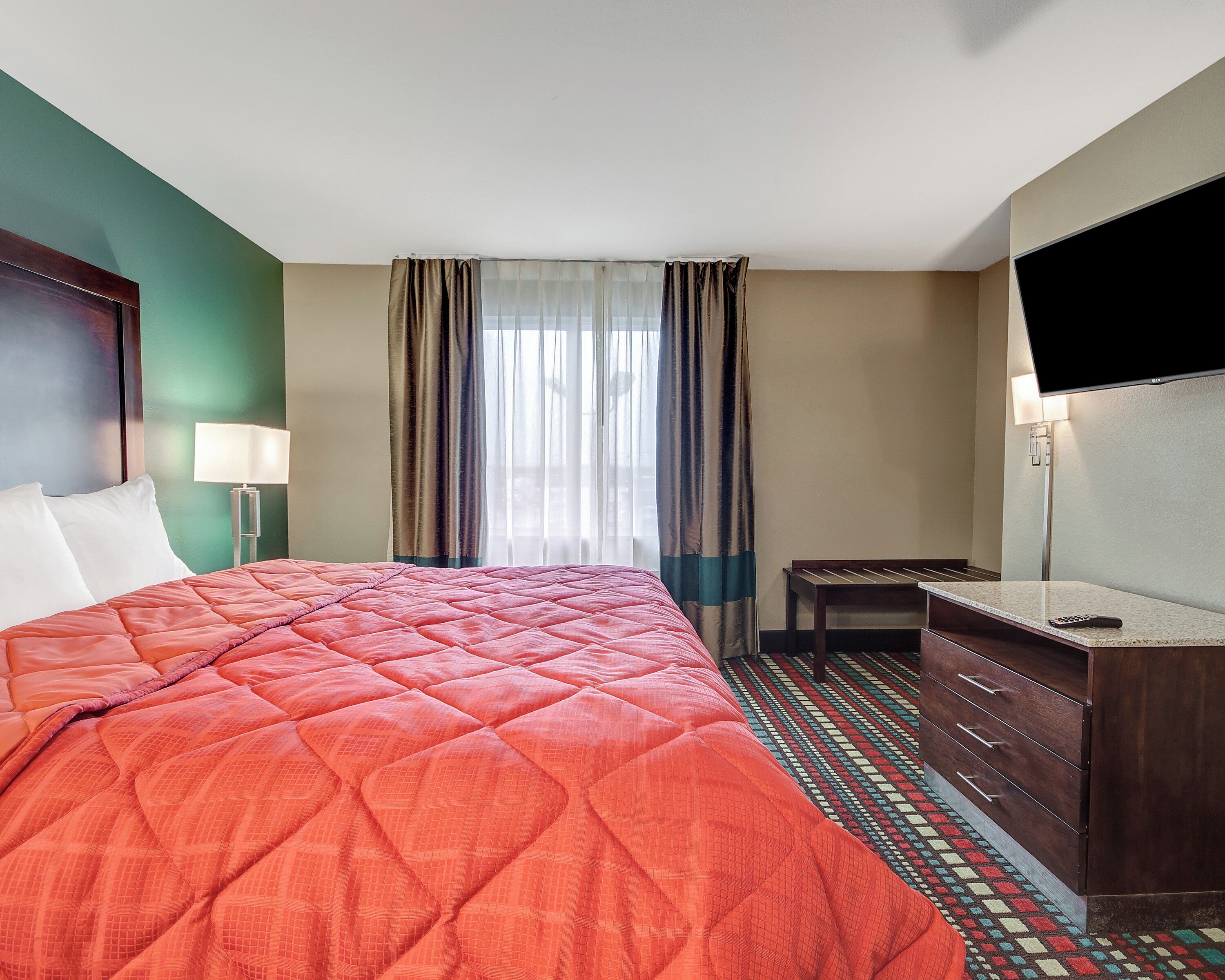 A hotel room with a large bed, a TV, a desk, and a dresser.