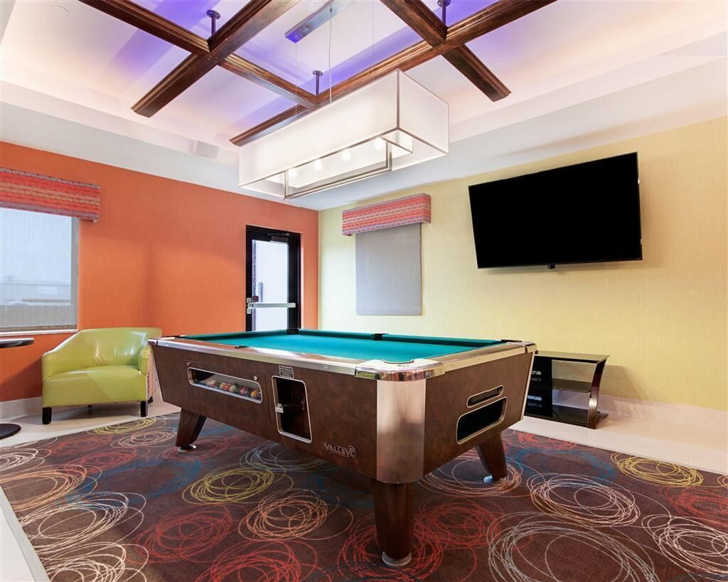 Une table de billard dans une pièce aux murs orange, avec une chaise verte et un téléviseur accroché au mur.