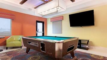 Une table de billard dans une pièce aux murs orange, avec une chaise verte et un téléviseur accroché au mur.