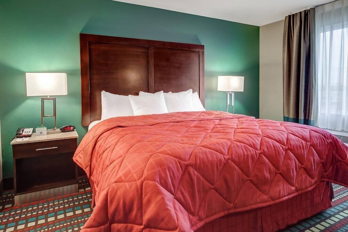 A hotel room with a large bed, two bedside lamps, a nightstand with a phone, and a window with curtains.