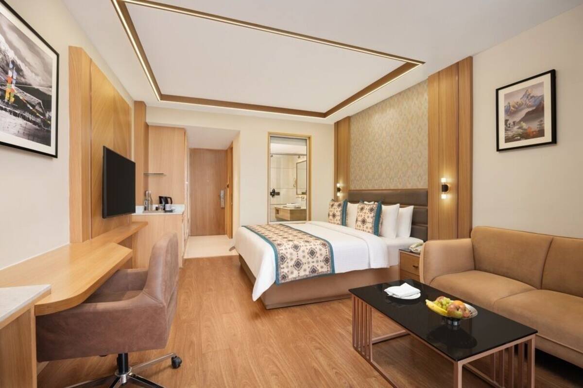 Quarto de hotel com cama, escrivaninha, cadeira, sofá, televisão e espelho.