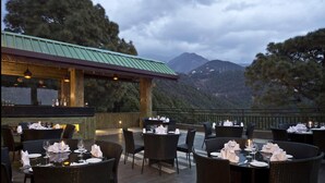 An outdoor dining area with tables set for two, overlooking a mountainous landscape. - Fortune Park Moksha, Mcleodganj  - Member ITC Hotels' Group (Dharamshala)