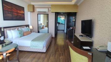 A hotel room with a bed, bedside table, lamp, television, and a desk with a chair.