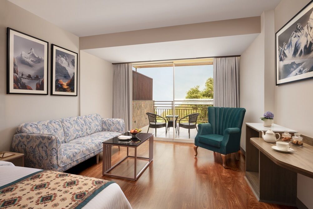 A hotel room with a sofa, a small table, a chair, a desk, and a balcony with outdoor furniture.