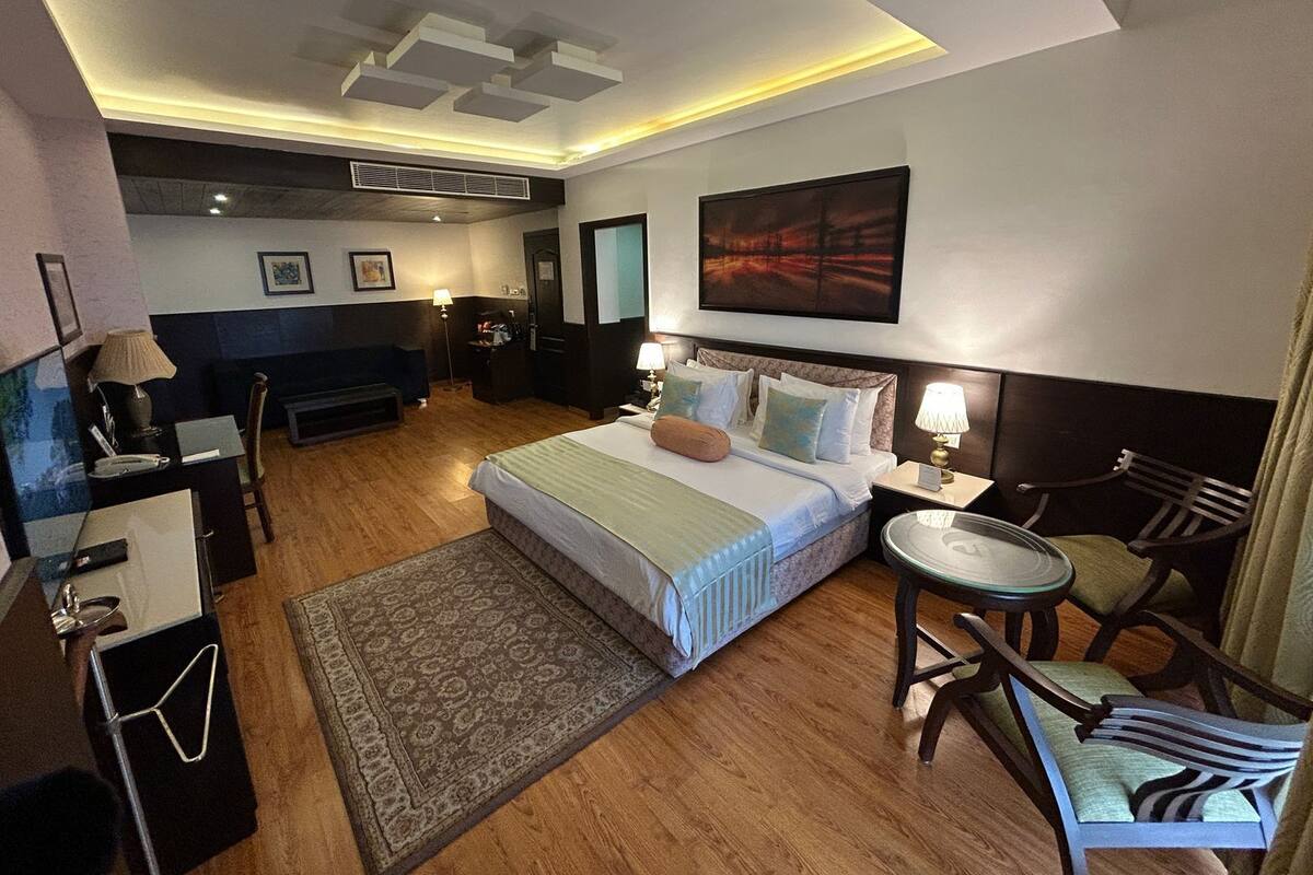 Ein Hotelzimmer mit Bett, Nachttisch, Sessel, Schreibtisch, Lampe und einem Kunstwerk an der Wand.