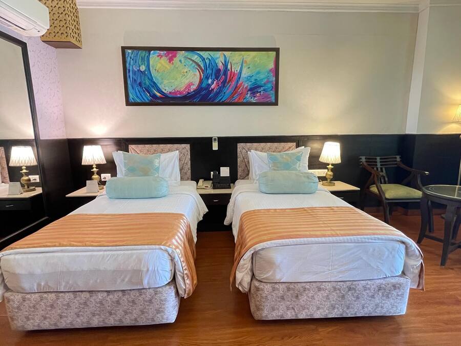 A hotel room with two beds, a desk, a chair, a lamp, and a painting on the wall.