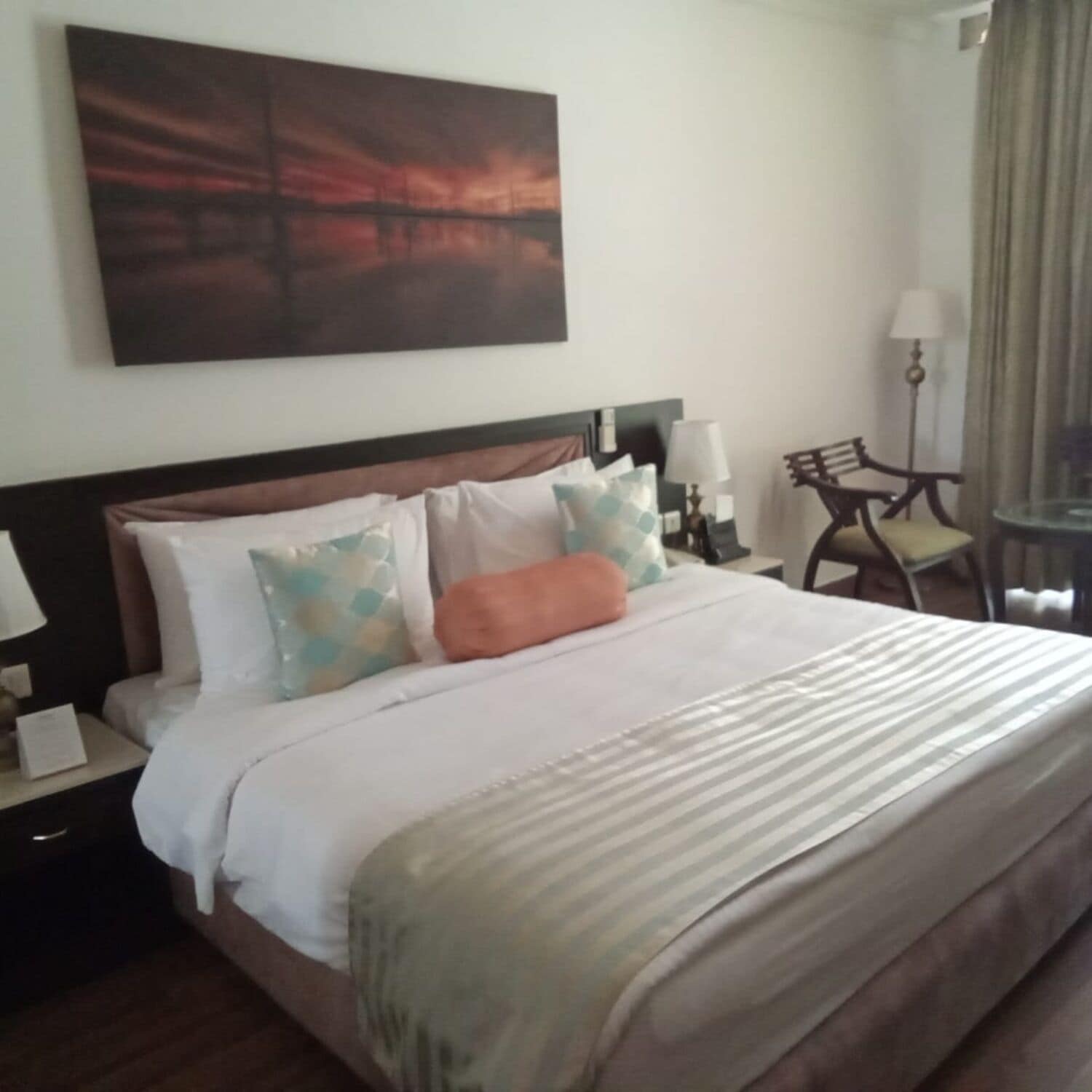 A hotel room with a bed, nightstands, a lamp, a chair, and a painting on the wall.