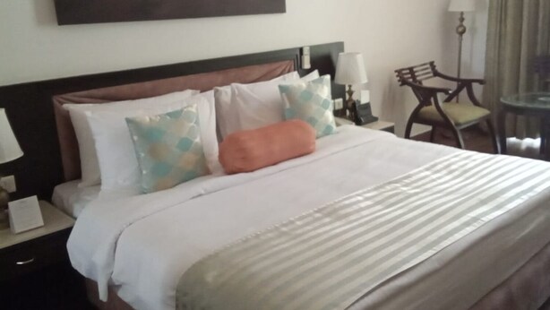 Une chambre d’hôtel avec un lit, des tables de chevet, une lampe, une chaise et un tableau au mur.