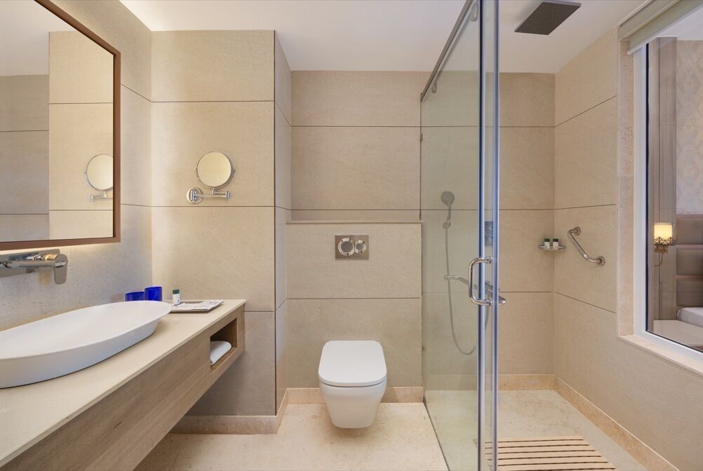 Une salle de bain moderne avec une douche à parois de verre, des toilettes blanches et un grand miroir.