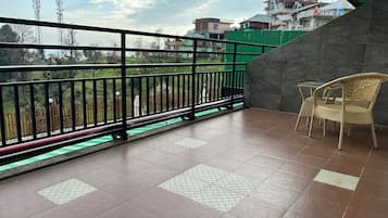 Un balcón con suelo de baldosas, baranda de metal negro y una silla de mimbre.